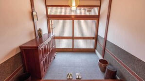 A traditional Japanese room with tatami flooring, a wooden cabinet, a sliding door, and a hanging light fixture. - Guest House IROHA Lotusland (Kaga)