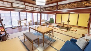 A traditional Japanese-style room with tatami flooring, a low table with chairs, a sofa, and a green chair. - Guest House IROHA Lotusland (Kaga)
