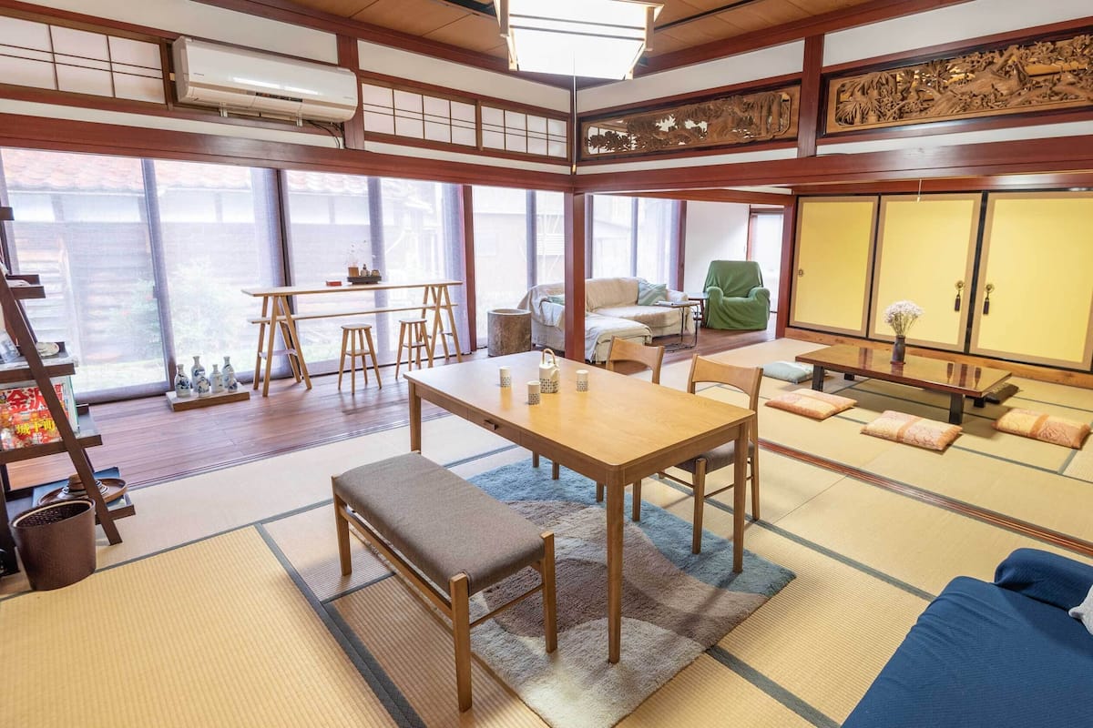 Une pièce de style japonais traditionnel, avec un sol recouvert de tatamis, une table basse entourée de chaises, un canapé et un fauteuil vert.