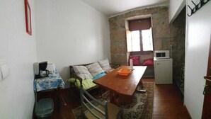 Un espacio habitable compacto con una mesa de comedor, un sofá, una pequeña cocina con microondas y un ventanal que proporciona luz natural.