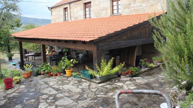 Una casa de piedra con techo de tejas, un patio cubierto con macetas y un suelo de piedra.