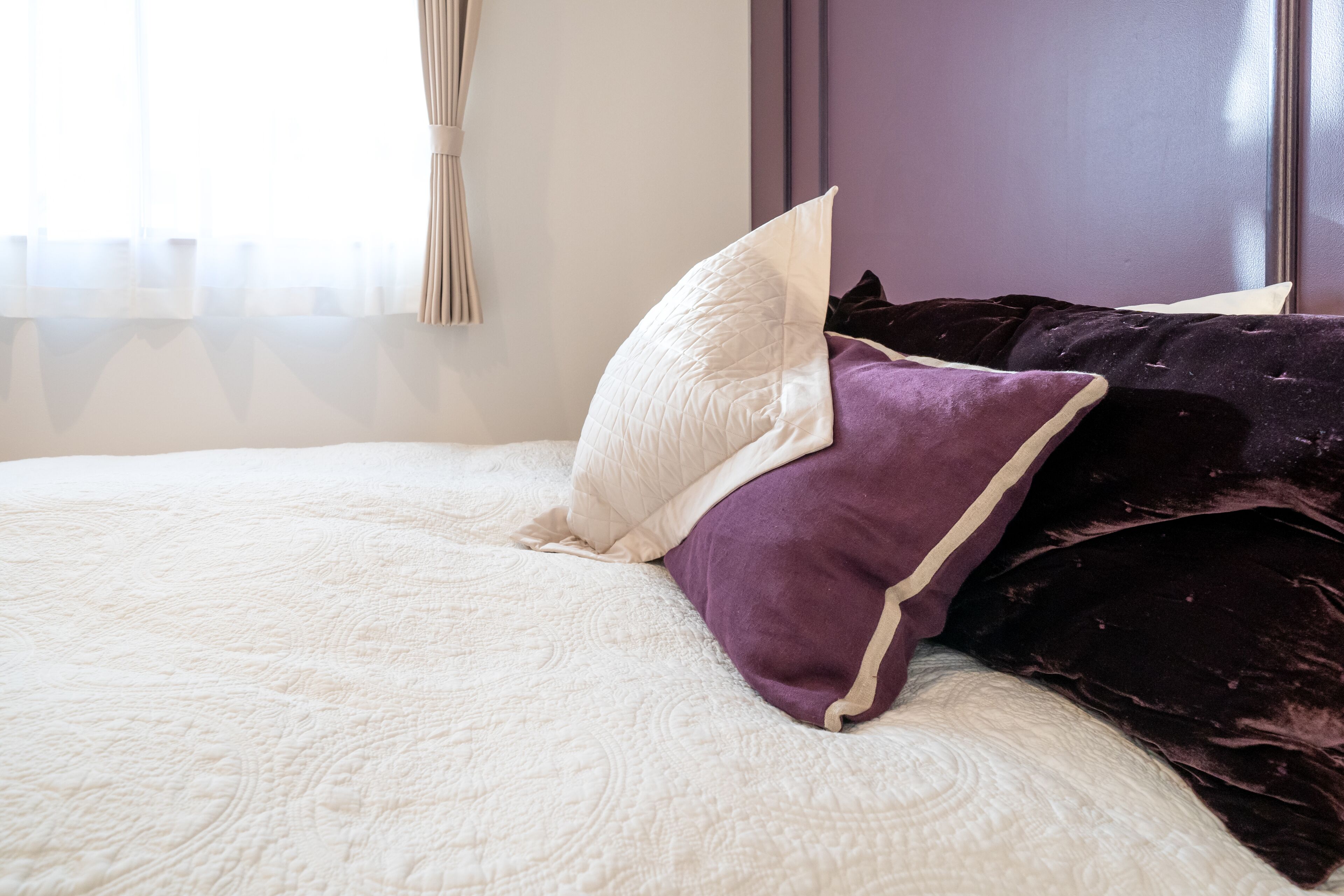 Ein Bett mit weißer Bettdecke und mehreren Kissen, darunter ein weißes und ein violettes.