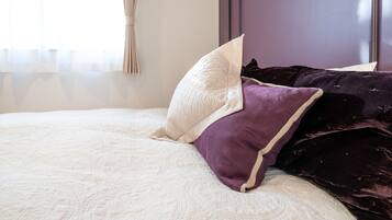 A bed with a white quilt and multiple pillows, including a white and a purple one.