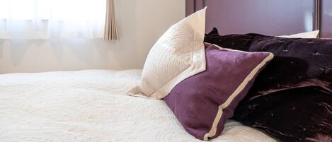 Ein Bett mit weißer Bettdecke und mehreren Kissen, darunter ein weißes und ein violettes.