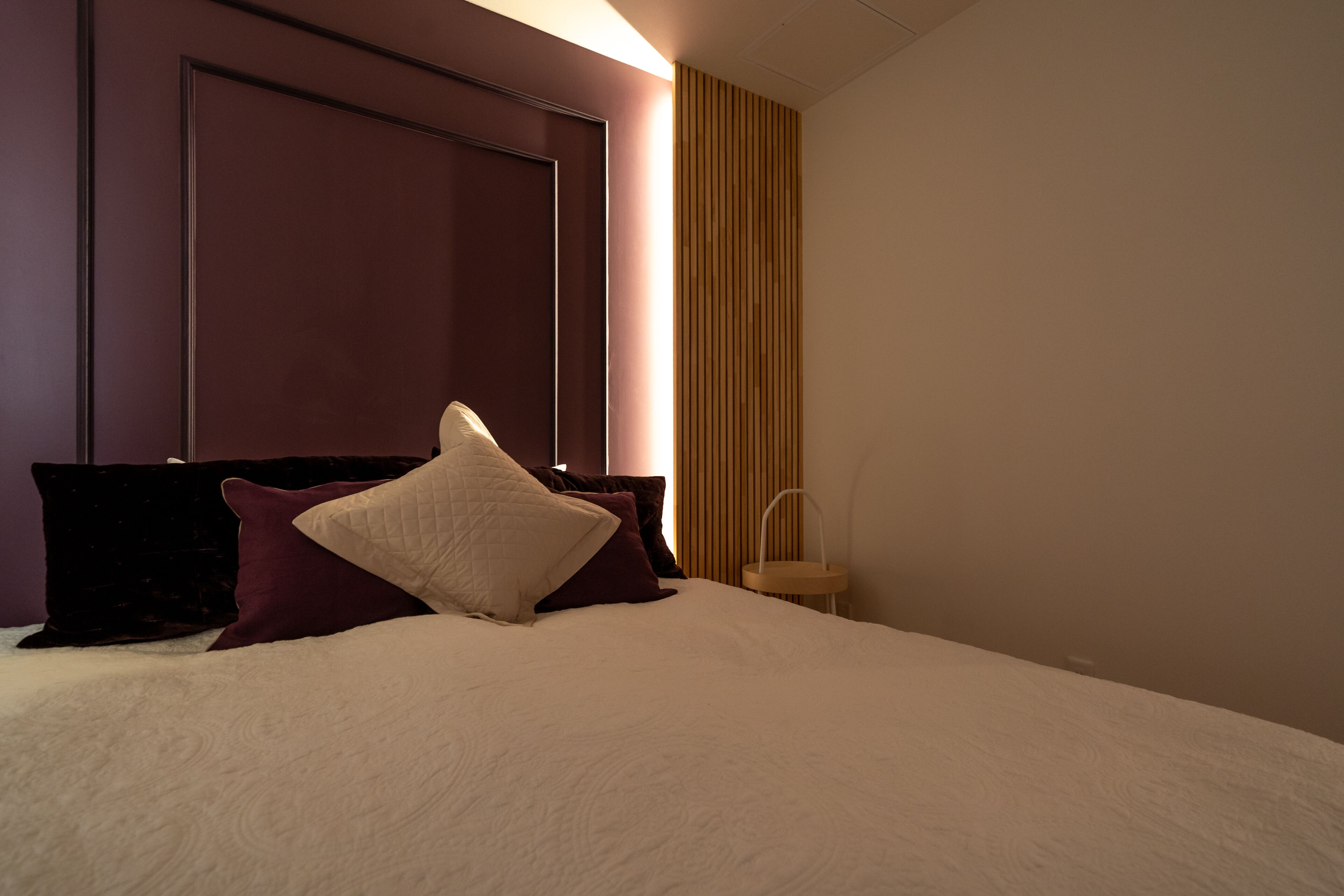 A neatly made bed with a white comforter and several pillows, a wooden headboard, and a small bedside table with a lamp.