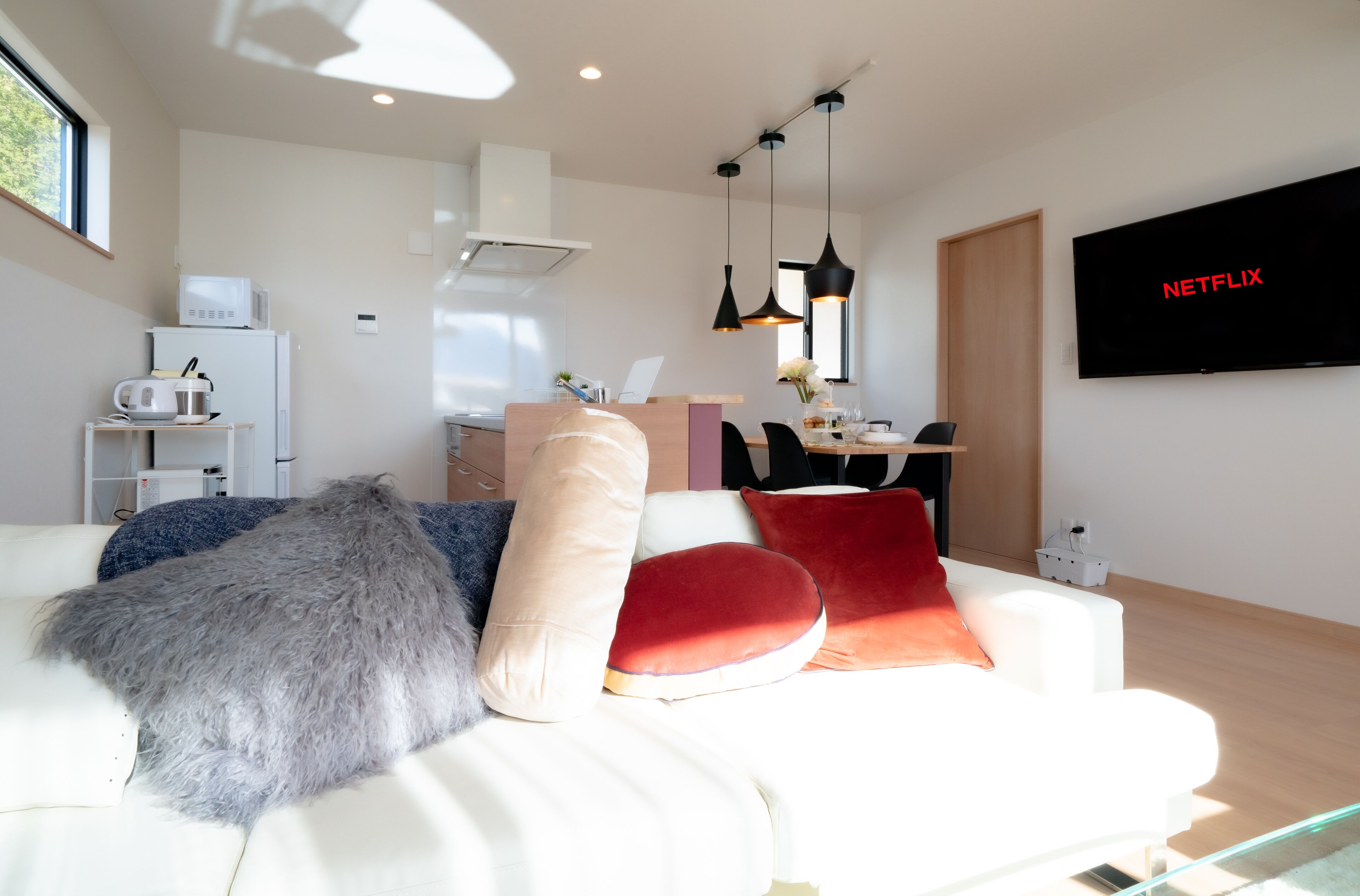 Un salon moderne avec un canapé blanc, des coussins rouges et beige, un plaid gris moelleux et un téléviseur à écran plat affichant le logo « NETFLIX ».