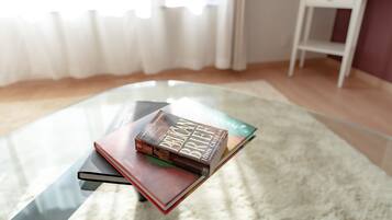 A glass table with books, a white side table, and a window with curtains.