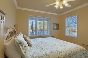 A bedroom with a bed, a ceiling fan, and two windows with blinds.