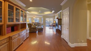 A spacious living room with hardwood flooring, built-in wooden cabinets, and a large window offering a view of the outdoors.