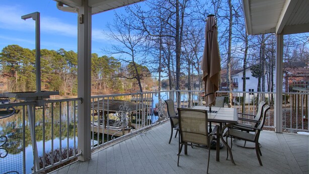 A covered outdoor area with a table and chairs, overlooking a body of water and trees.
