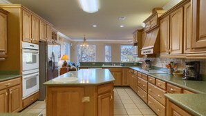 A spacious kitchen with wooden cabinets, a large island, and a view of the outside through the windows.