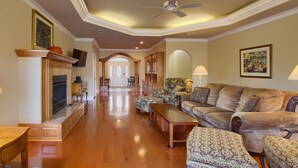 A spacious living room with a fireplace, a ceiling fan, and a large window.