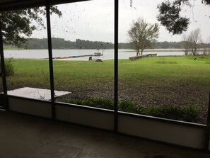 A view through large windows of a grassy area with a dock and a boat. - Florida Lakeside Getaway  (Hawthorne)