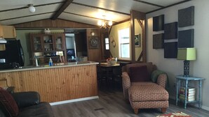 Ein gemütliches Wohnzimmer mit einer Holztrennwand, einem gemusterten Sessel und einem Essbereich mit Tisch und Stühlen.
