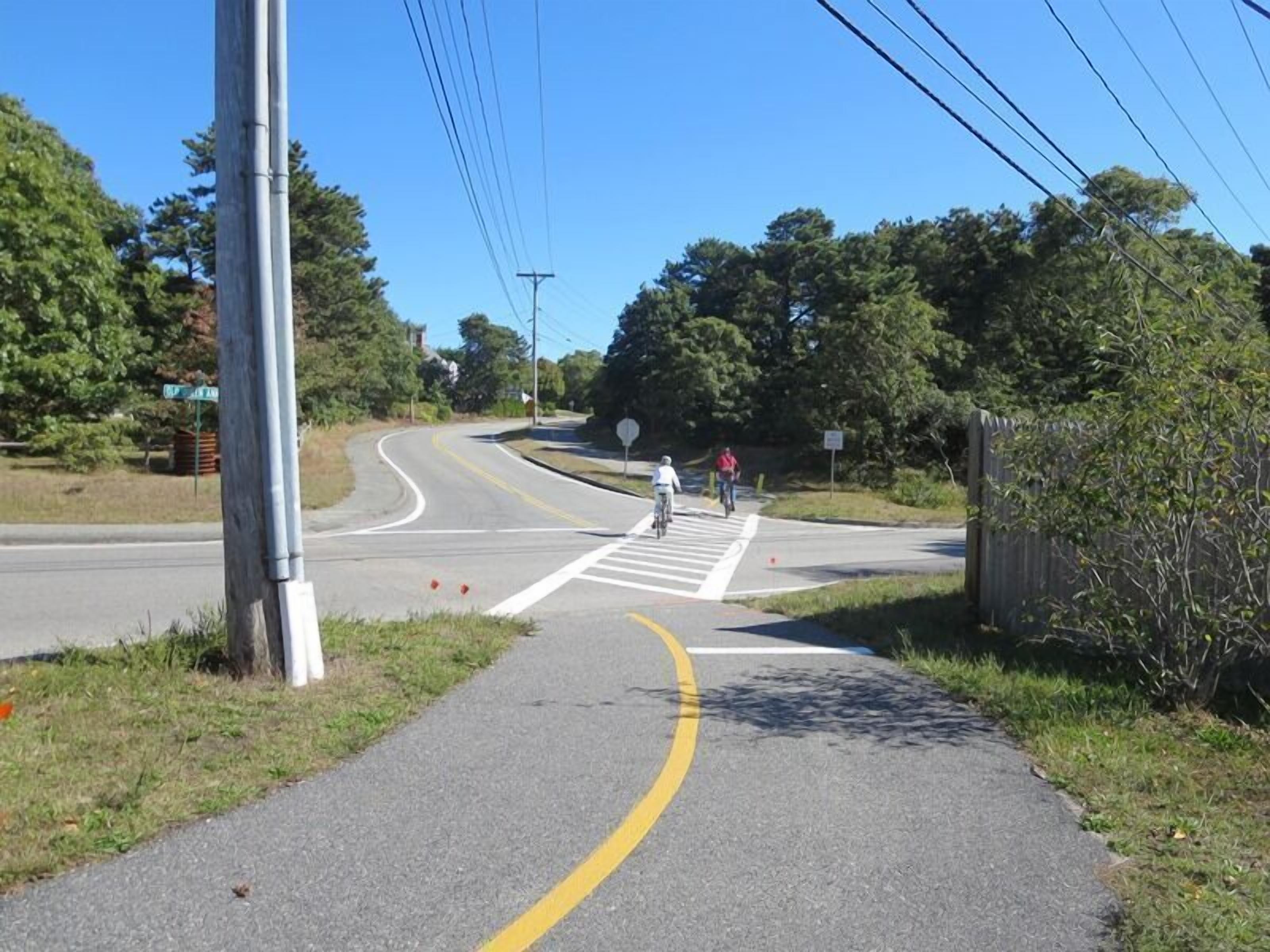 Una carretera con carril bici, paso de peatones y una curva más adelante.