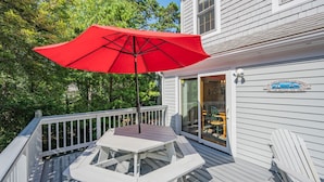 Une terrasse avec un parasol rouge, une table et des chaises.