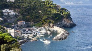 Un pueblo costero con un puerto deportivo, edificios en una ladera y un litoral rocoso.
