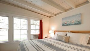 Een slaapkamer met een groot bed, een schilderij van zeilboten aan de muur en een raam met gordijnen.