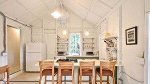 Een keuken met een centraal eiland, vier houten stoelen, een koelkast en diverse keukenapparaten.