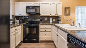Kitchen features a central stove, microwave, and sink, with white cabinetry and a granite countertop.