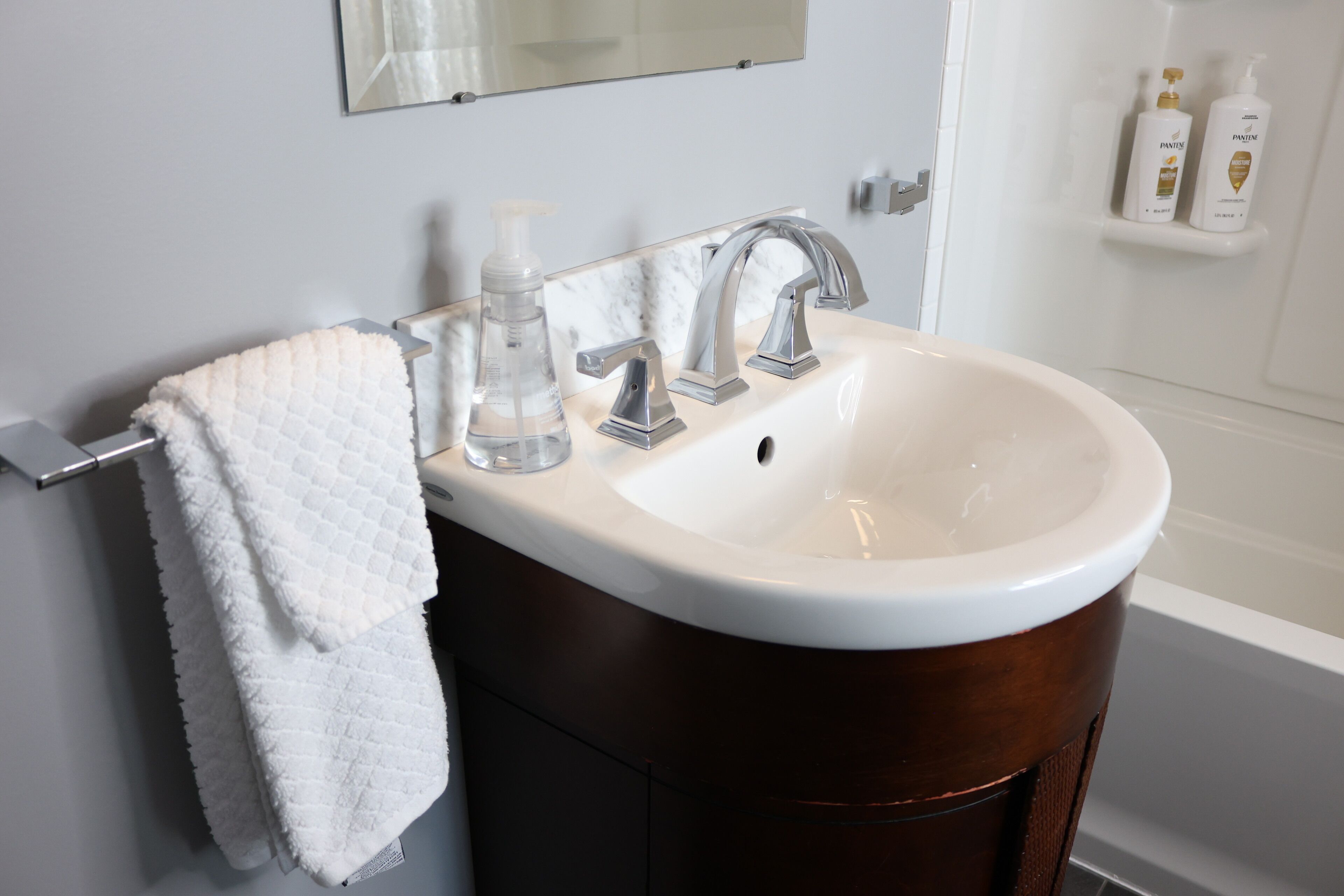A bathroom with a white sink, two faucets, a towel rack with a white towel, and a mirror above the sink.