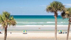 Una playa con palmeras, sombrillas y una vista despejada del océano.