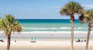 A beach with palm trees, clear blue water, and a few umbrellas.