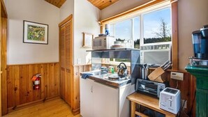 A compact kitchen with wooden walls, a microwave, a kettle, and a toaster. - Deer Harbor Cottage on the Bluff (Eastsound)