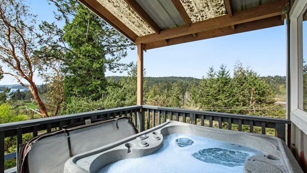 A hot tub on a covered deck with a view of trees and hills. - Deer Harbor Cottage on the Bluff (Eastsound)
