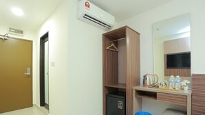A hotel room with a wooden wardrobe, a small refrigerator, a desk with a mirror, and a blue trash bin. - Bitz Bintang Hotel (Kuala Lumpur)