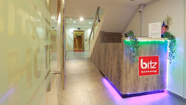 A hotel reception area with a wooden reception desk, a staircase, and a sign indicating the hotel name and level. - Bitz Bintang Hotel (Kuala Lumpur)