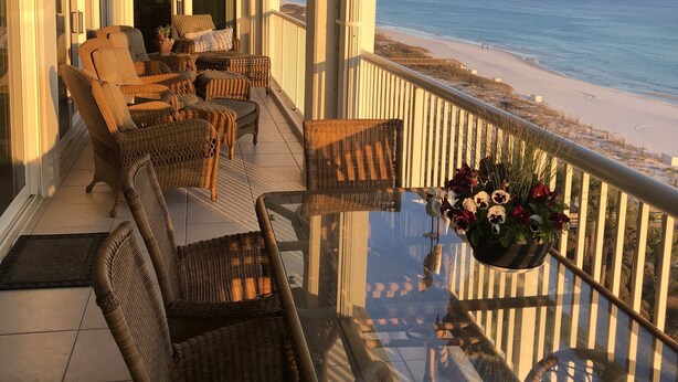 A balcony with wicker furniture, a glass table, and a view of the beach.