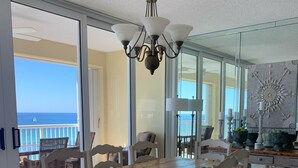 A dining area with a wooden table and white chairs, a chandelier, and a view of the ocean.