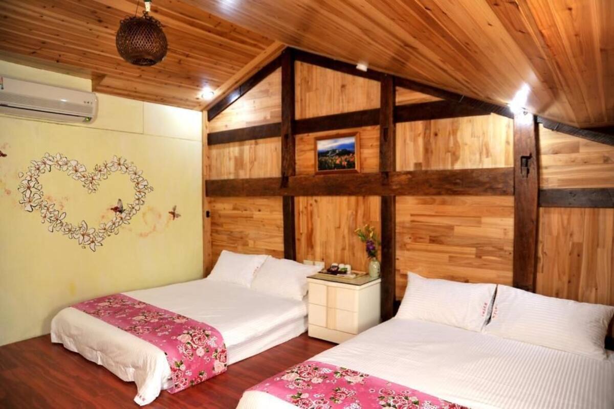 A room with two beds, wooden walls, a heart-shaped decoration, and a small table with a vase.