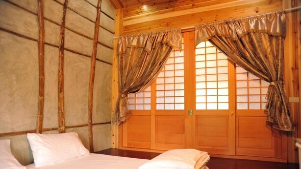 Una habitación de madera con una cama, un ventanal y una puerta.