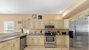 A kitchen with beige cabinets, stainless steel appliances, and a window with blinds.