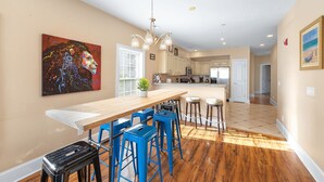 A modern kitchen with a long island, blue bar stools, and a large painting on the wall.