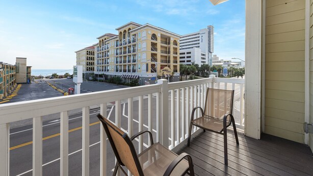 A balcony with two chairs, a view of a multi-story building, and a parking lot.