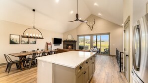 A spacious kitchen with a large island, a ceiling fan, and a fireplace. - *NEW w/ VIEWS* | Modern Mtn. Townhome minutes from RMNP, WP, & Granby Ranch! (Granby)