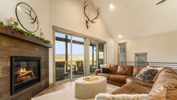 A spacious living room with a fireplace, leather sofa, and a large window offering a view of the outdoors. - *NEW w/ VIEWS* | Modern Mtn. Townhome minutes from RMNP, WP, & Granby Ranch! (Granby)