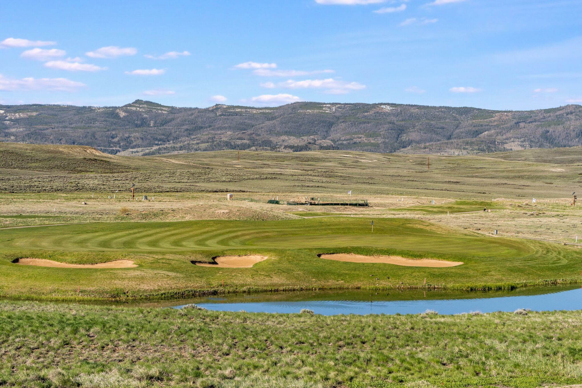 Un campo de golf con un estanque, búnkeres de arena y un paisaje montañoso de fondo.