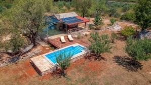 En avskild villa med en swimmingpool, utomhusmöbler och en byggnad som drivs med solenergi.