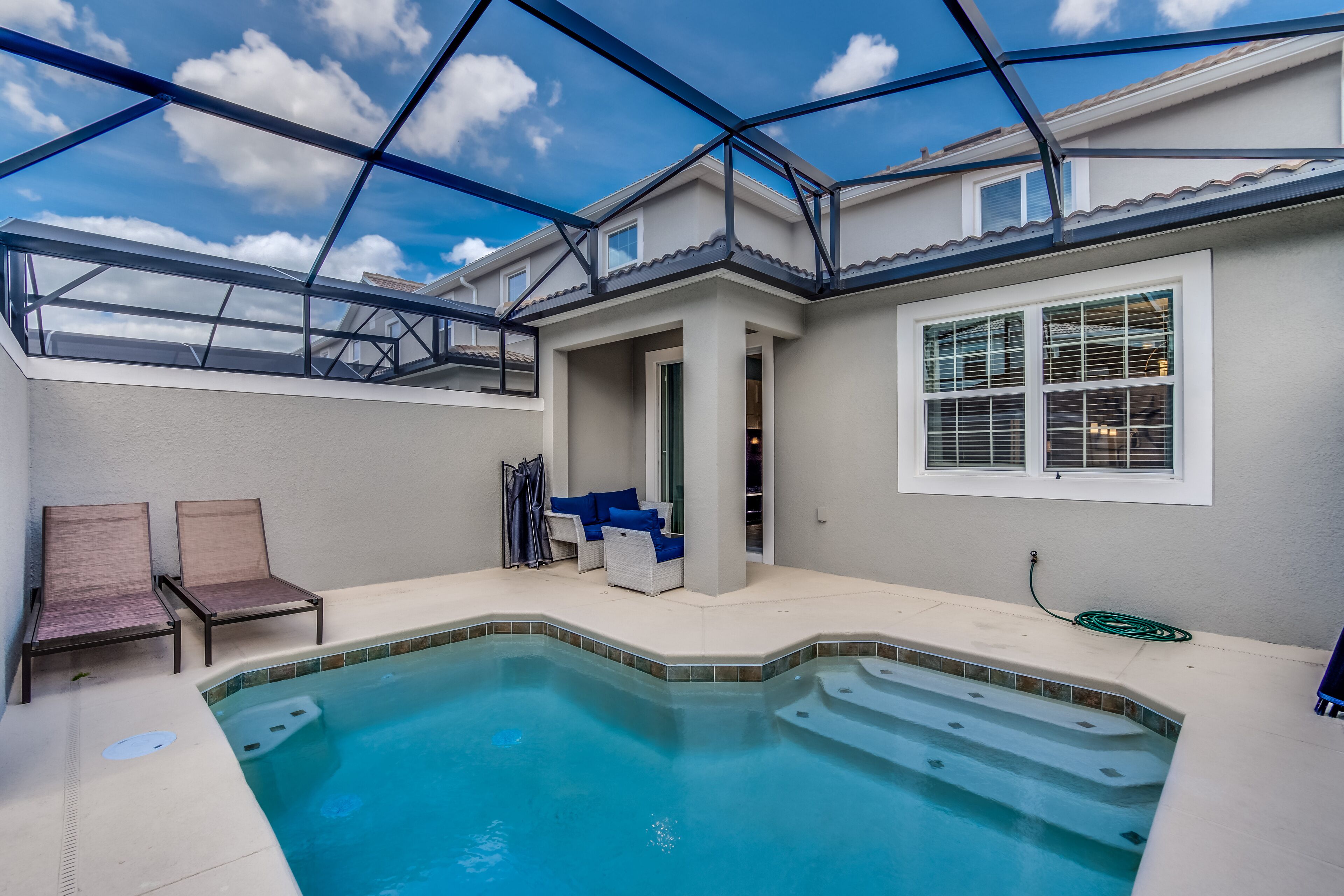 A swimming pool with a glass ceiling, two lounge chairs, and a covered seating area with blue cushions.