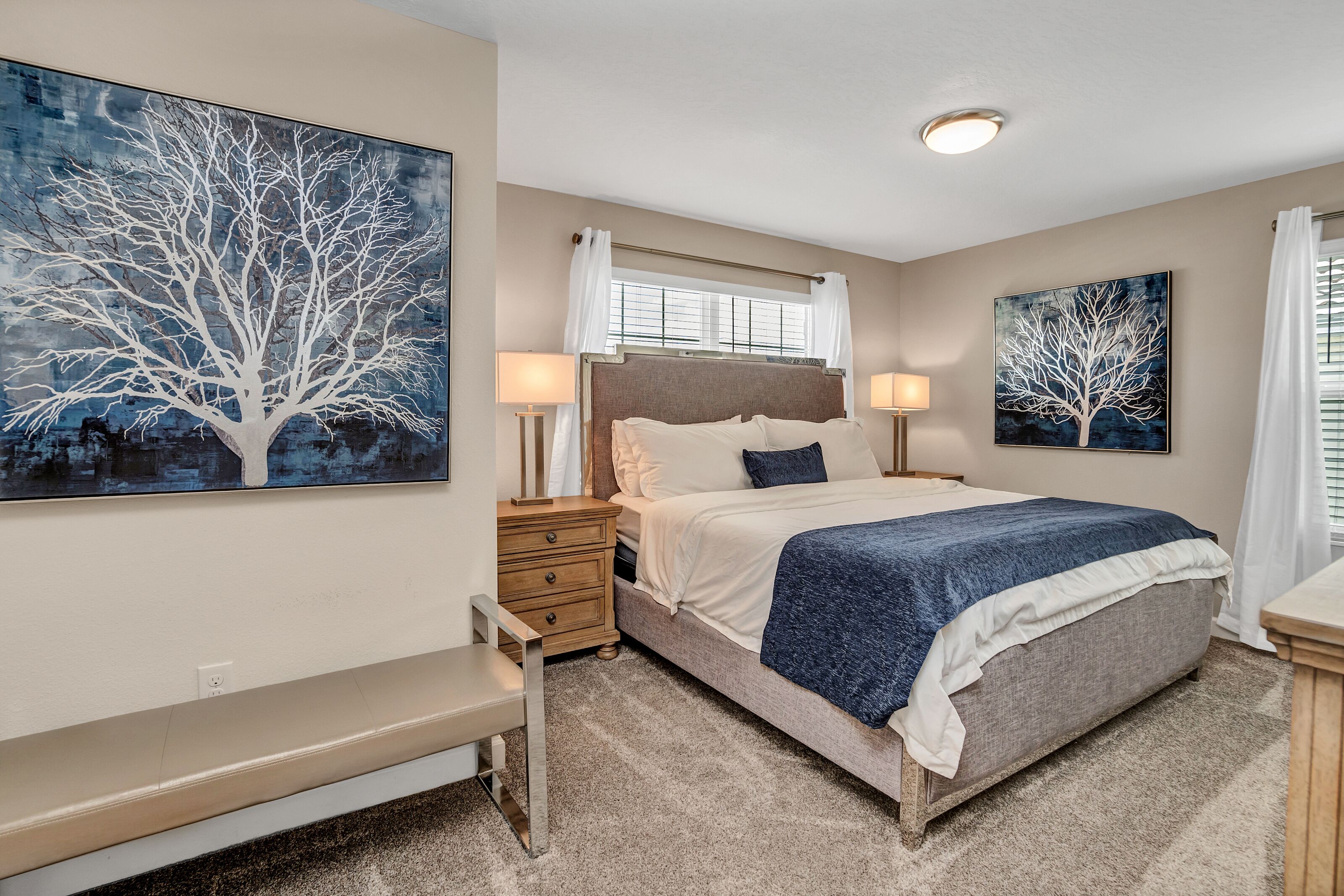 Ein Schlafzimmer mit einem großen Bett, Nachttischen, einer Bank und zwei an der Wand befestigten Bildern von einem Baum.