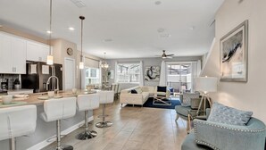 A modern kitchen with a central island, bar stools, and a dining area with a sofa and coffee table.