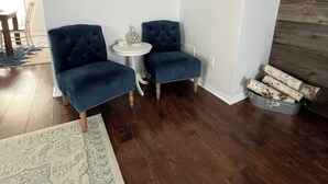 Une pièce avec deux fauteuils bleus, une petite table ronde, un tableau encadré au mur et un plancher en bois.
