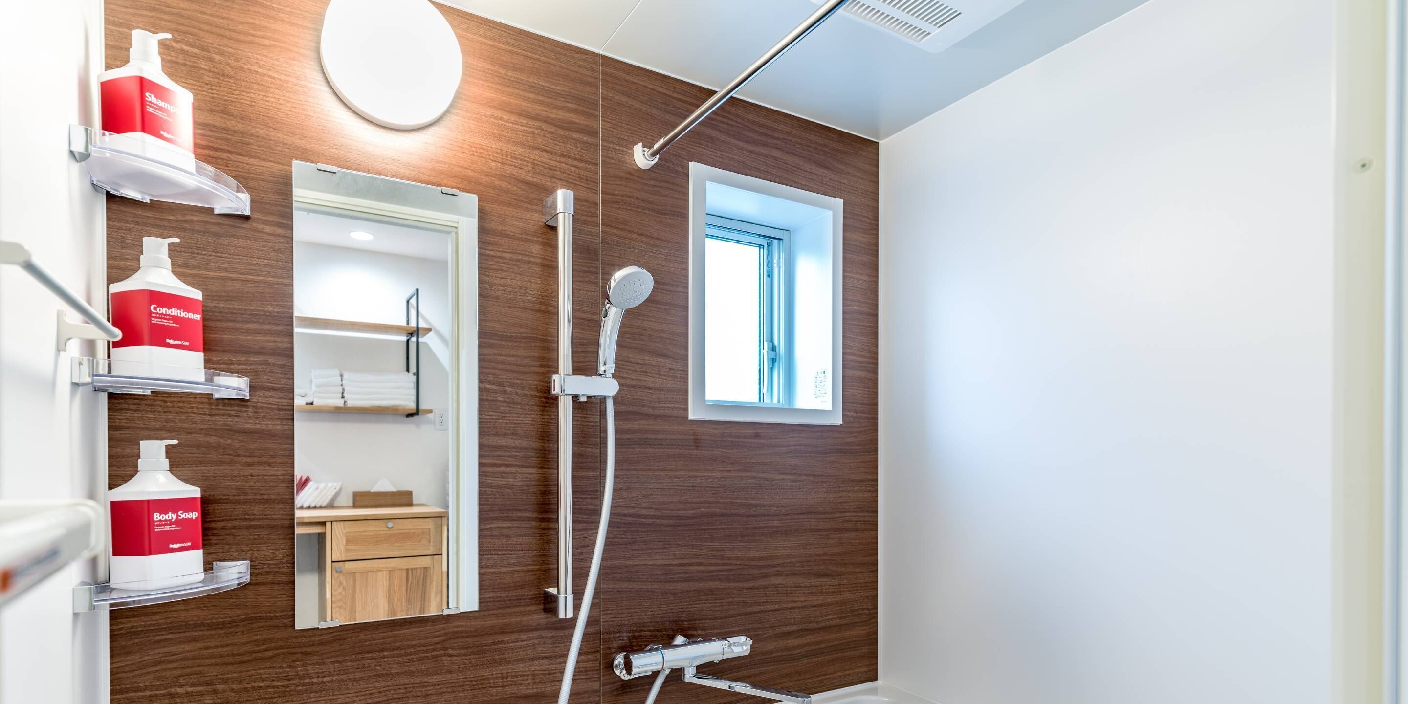 A modern bathroom with a wooden wall, a mirror, a shower, and shelves with toiletries.