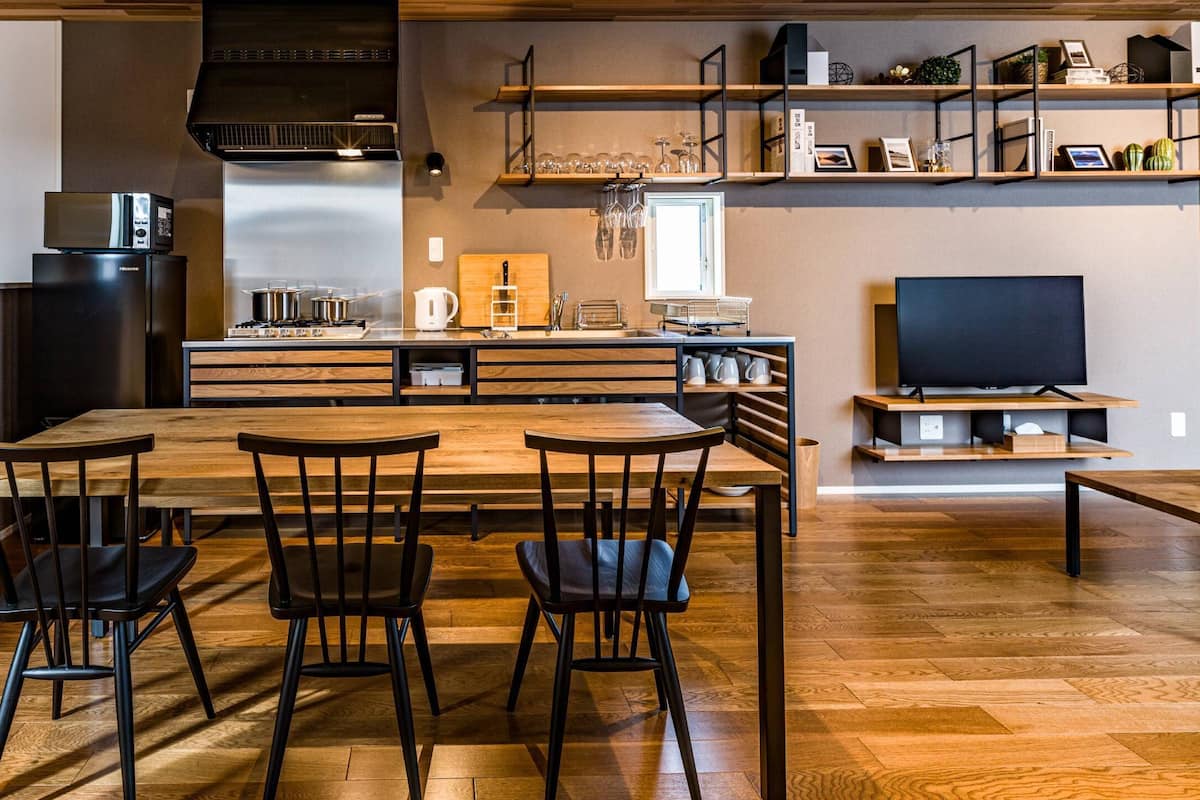A modern kitchen with a central island, wooden flooring, and black chairs.