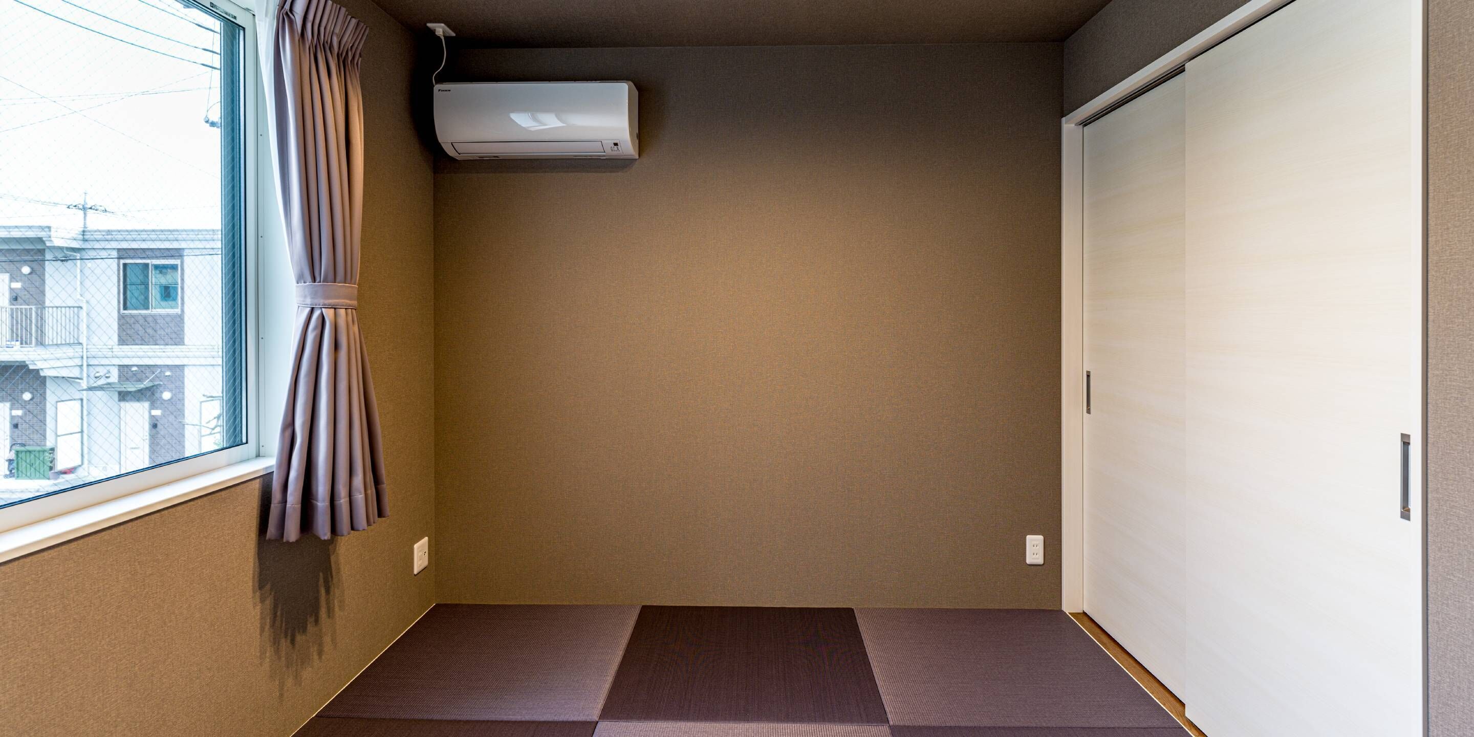A room with a sliding door, a window with curtains, a wall-mounted air conditioner, and a tatami mat floor.