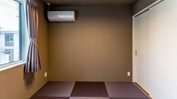 A room with a sliding door, a window with curtains, a wall-mounted air conditioner, and a tatami mat floor.